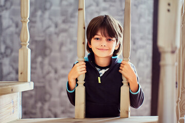 Smiling 7 year old male child looks through balusters of railing on wooden staircase.