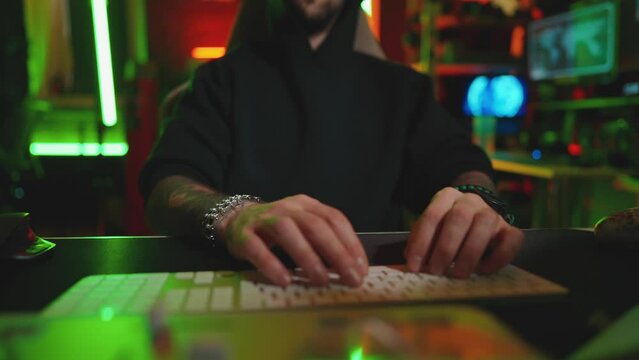 Hacker writing code cracking computer. Man programmer in hoodie cracks system, using computer in dark room. Hacker attack, technology, virus infected software, dark web person, cyber security concept.