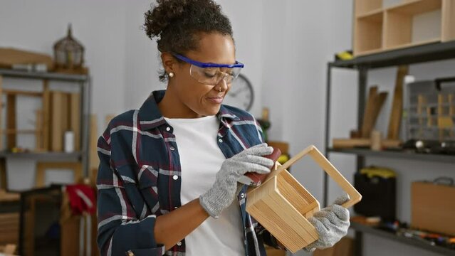 Smiling woman wearing safety goggles sands a wooden crate in a well-equipped carpentry workshop
