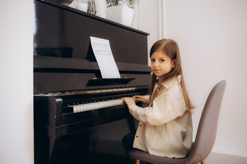 A nice little girl is playing on a big white piano. The concept of musical and aesthetic education...