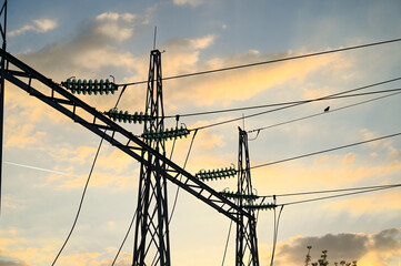 Electric poles and power lines at sunset. Transmission of electric power. High voltage electricity...
