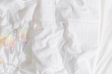 Two colored champagne glasses with rainbow color shadow on bed, on white sheets. Minimal lifestyle...