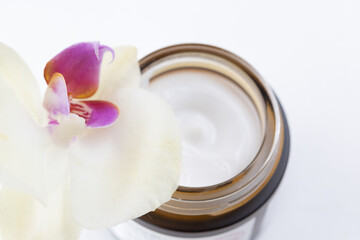 Cream in a jar, orchid flower on white defocused background, macro. Natural face cream, glass jar with face cream. Natural cosmetics product. Skincare and beauty concept. Mockup