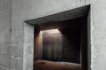 a dark room with concrete walls and a small light opening in the ceiling