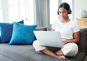 Woman, laptop and headphones for remote work on couch, check email and freelancer on website in...
