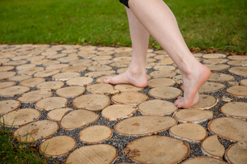 Tactile path in park, woman walks barefoot along eco path made of wood and small stones, strengthen...