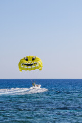 Parasailing in the sea. Yellow parachute with smiley face on sky background. Flying parachute with a smiley face