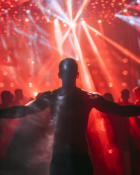 A man seen from back in a music event, dancing in neon color lights