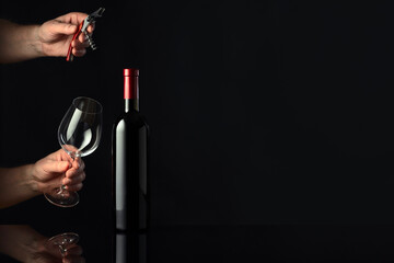 Bottle of red wine and hands with corkscrew and wine glass.