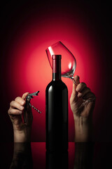 Unopened bottle of red wine and hands with corkscrew and wine glass.