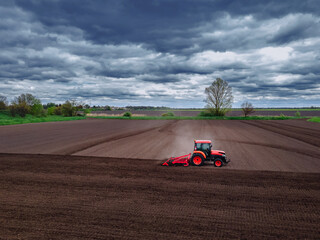 A red tractor working in the field. Agricultural red small tractor in the field plowing, works in the field. Tractor plows the field aerial view.