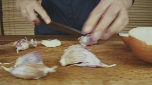 Woman's hands close up cutting onion and smashing, and peeling garlic on a wooden board with a big knife. Wooden kitchen table. . High quality 4k footage
