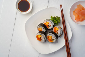Maki sushi on white plate.Japanese sushi rolls with salmon, cucumber, shrimp eggs and Imitation Crab Stick with soy sauce dip and chopsticks on white wood background.Top view