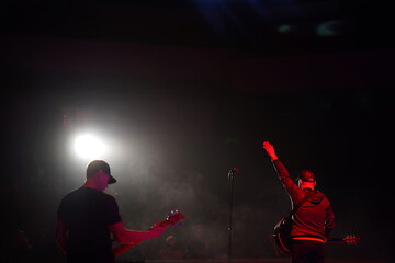 Rock band vocalist silhouette with the guitar singing to microphone with the hand raised up in red lights
