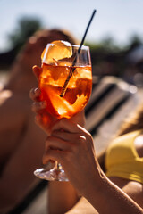Closeup of young womans hand with neat red manicure holds elegant glass with long stem of aperol. Tasty citrus cocktail with orange slice.