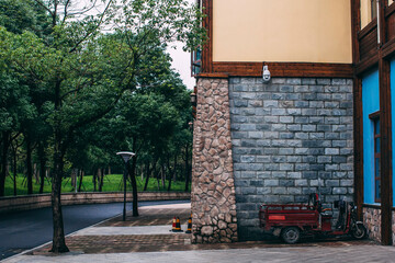 Brick wall of building in chinese park. Asphalt road, motorbike, trees.
