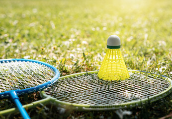 Two badminton rackets and yellow shuttlecock on the green grass. Summer leisure and sports activity.