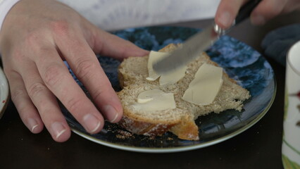 Close-up hand spreading butter on slide of bread for breakfast nutrition. Knife spreads buter on carb food