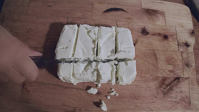 Close up ow woman's hands cutting fresh traditional white cottage cheese on a wooden plank. Indoor, studio shot, kitchen. High quality 4k footage
