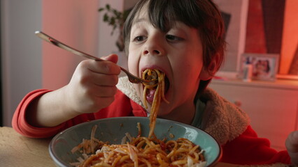 Little boy eating pasta, close-up face of 5 year old child twirling spinning spaghetti with fork by...