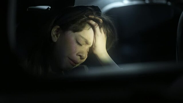 Teenage girl holds her head while crying in a the front seat of a dark car after a neglectful incident