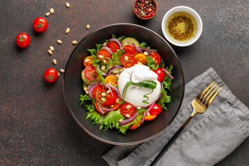 Salad with traditional italian burrata cheese. Burrata ball with cherry tomatoes, cucumber slices, onion  and pine nut in bowl on the table. Top view