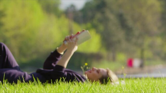 Young Woman is Reading Book on Grass in Nature