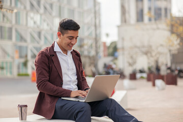 Young man sitting on stairs using a laptop with buildings in the background.
