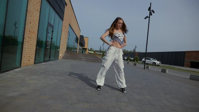 Woman gracefully dancing in high heels in front of urban building. Slow motion shooting. Energetic woman performing dance routine outdoors. Dancer expressing joy in city backdrop. Female dancer 
