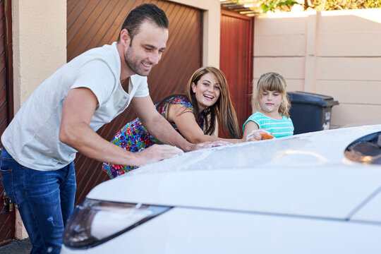 Family, Wash And Cleaning Car Together In Driveway For Chores Or Outdoor Activity, Learning And Responsibility. Mom, Dad And Child With Cloth, Soap And Sponge For Teamwork For Scrubbing Vehicle.