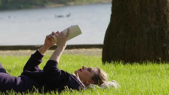 Young Woman is Reading Book on Grass in Nature