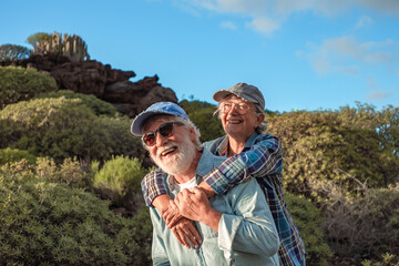 Cheerful caucasian senior couple with backpack and cap enjoying trekking day in countryside admiring landscape, Healthy lifestyle in retirement concept