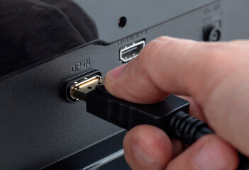 Close-up of a hand plugging a DisplayPort cable into the connector DP-IN. Insert the DisplayPort...