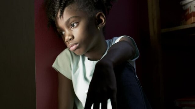 Tight shot of a young sad girl hiding in a dark room