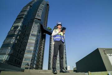 Skilled engineer operating tablet to manage HVAC machinery on top of building, urban architecture in distance.