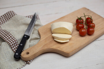 Sliced mozzarella cheese with tomatoes on a cutting board, on a white wooden background