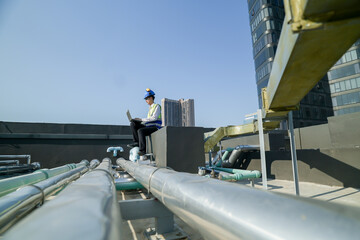 Engineer on building rooftop with laptop, overseeing urban construction, blue sky, and skyscrapers.