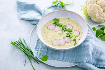 Creamy white cauliflower soup with radish and chives, healthy food with herbs