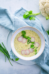 Creamy white cauliflower soup with radish and chives, healthy food with herbs