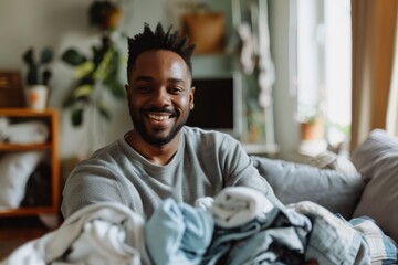 Adult male with a warm smile surrounded by laundry in a comfortable indoor environment