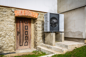 Air source heat pump installed outside of old renovated house, green renewable energy concept of...