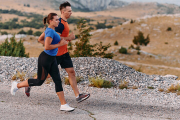 A couple dressed in sportswear runs along a scenic road during an early morning workout, enjoying the fresh air and maintaining a healthy lifestyle
