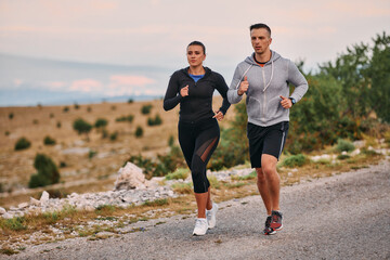 A couple dressed in sportswear runs along a scenic road during an early morning workout, enjoying the fresh air and maintaining a healthy lifestyle