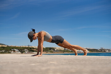 Sultry Brunette Athlete in Sportswear and Baseball Cap Training by the Sea