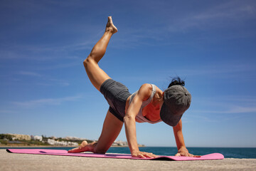 Brunette Woman Performing Isometric Exercises on Pink Exercise Mat by the Sea