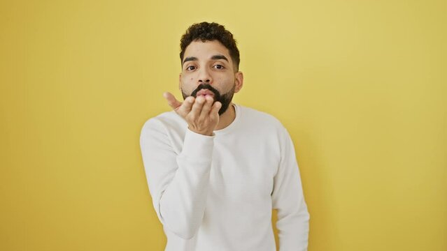 Young man standing looking at the camera blowing a kiss with hand on air being lovely and sexy. love expression. over isolated yellow background
