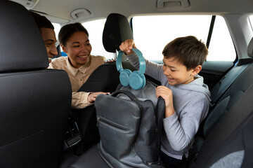 Preteen boy putting headphones in his backpack, parents turning back and looking at son, coming to...