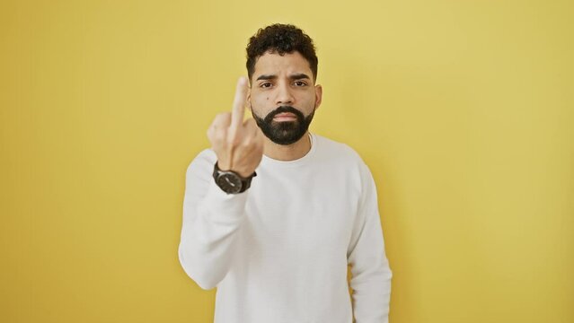 Young latin man flashing a rude, impolite 'fuck you' gesture, standing isolated on a vibrant yellow backdrop. a provocative show-off with a naughty expression.