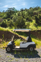 Leisure day on the course: white golf cart parked against a lush green hill under the bright sunny sky