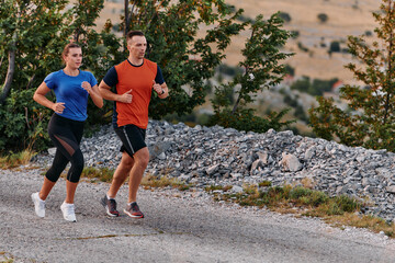 A couple dressed in sportswear runs along a scenic road during an early morning workout, enjoying the fresh air and maintaining a healthy lifestyle